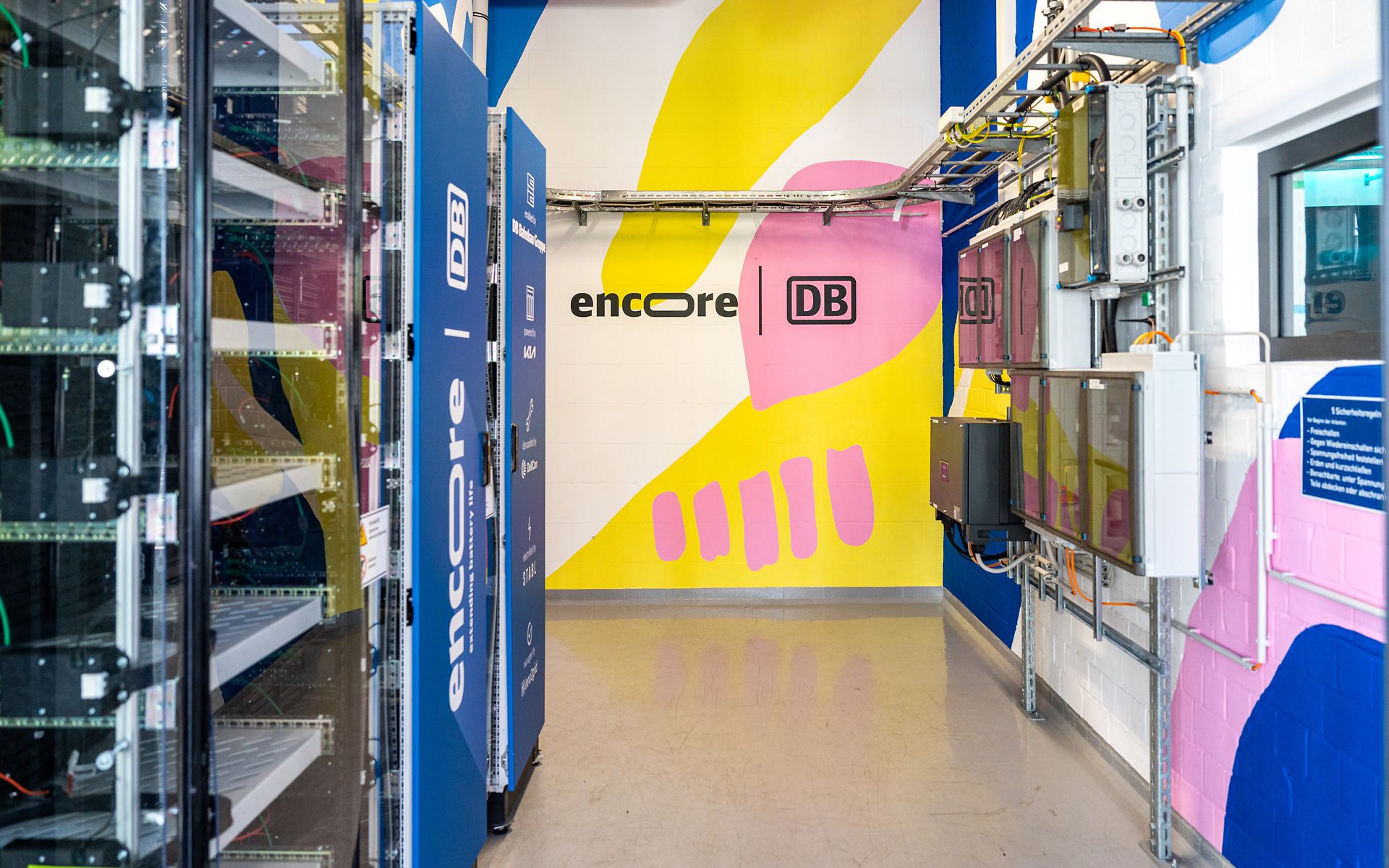 Batteriespeicher von encore | DB auf dem EUREF-Campus vor bunt bemalter Wand.