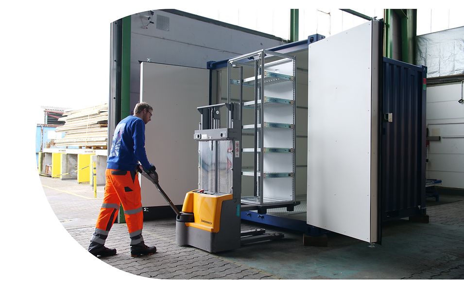Mitarbeiter von encore | DB hebt mit einem elektrischen Hubwagen ein Lastenregal in einen leeren 20-Fuß-Container. 
