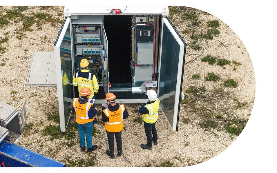 Vier Personen mit Warnwesten stehen von einem geöffneten encore | DB Batteriespeicher.