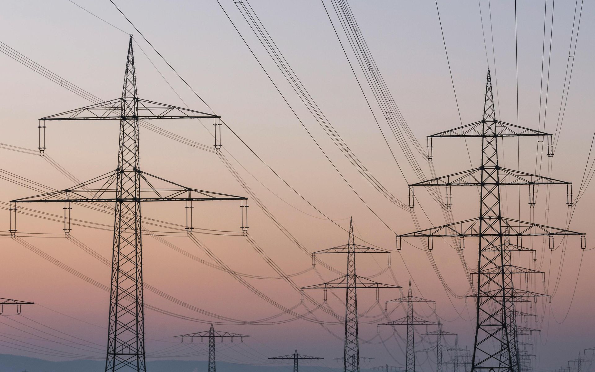Mehrere Strompfeiler und Hochspannungsleitung vor Abendhimmel.