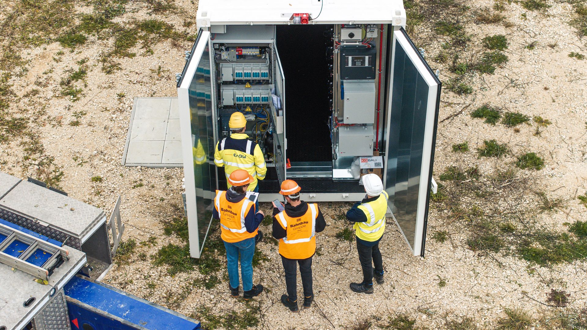 Luftaufnahme von vorn, geöffneter Batteriespeicher, 4 Mitarbeitende