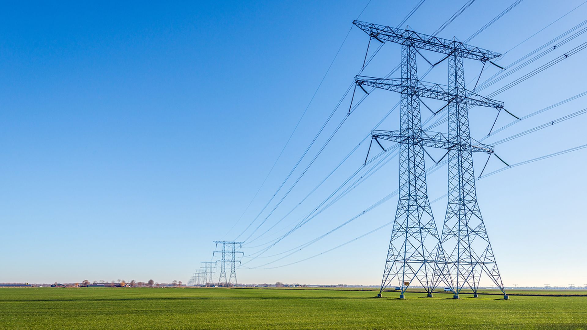 Strommasten auf grünen Feldern vor blauem Himmel